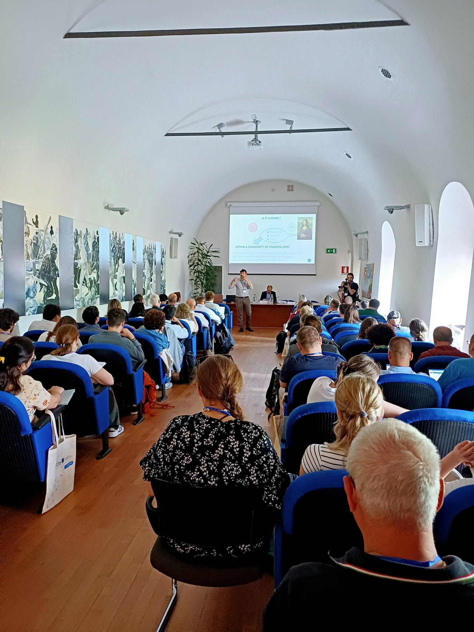 Pubblico seduto durante un convegno in una sala con volta a botte