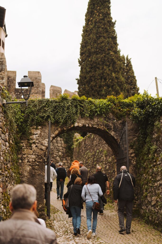 Gruppo di visitatori sotto un arco in pietra coperto d'edera, sulla salita al castello