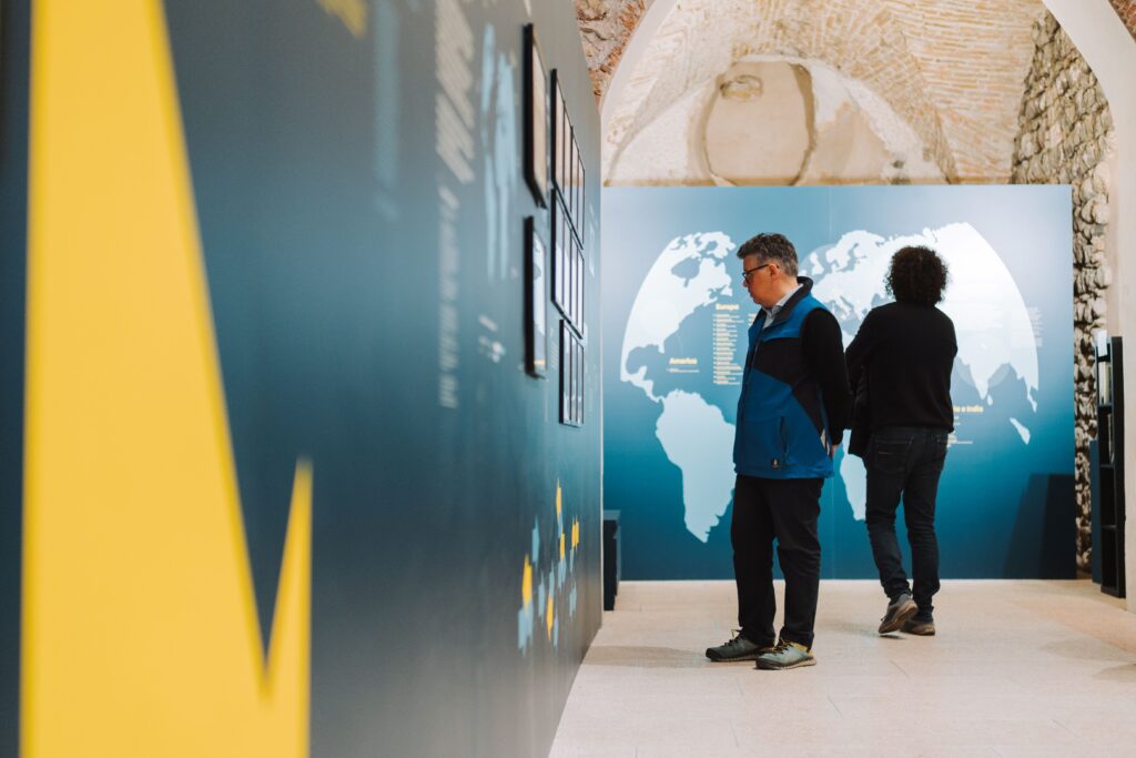 Due visitatori davanti a una parete con un mappamondo in una sala espositiva