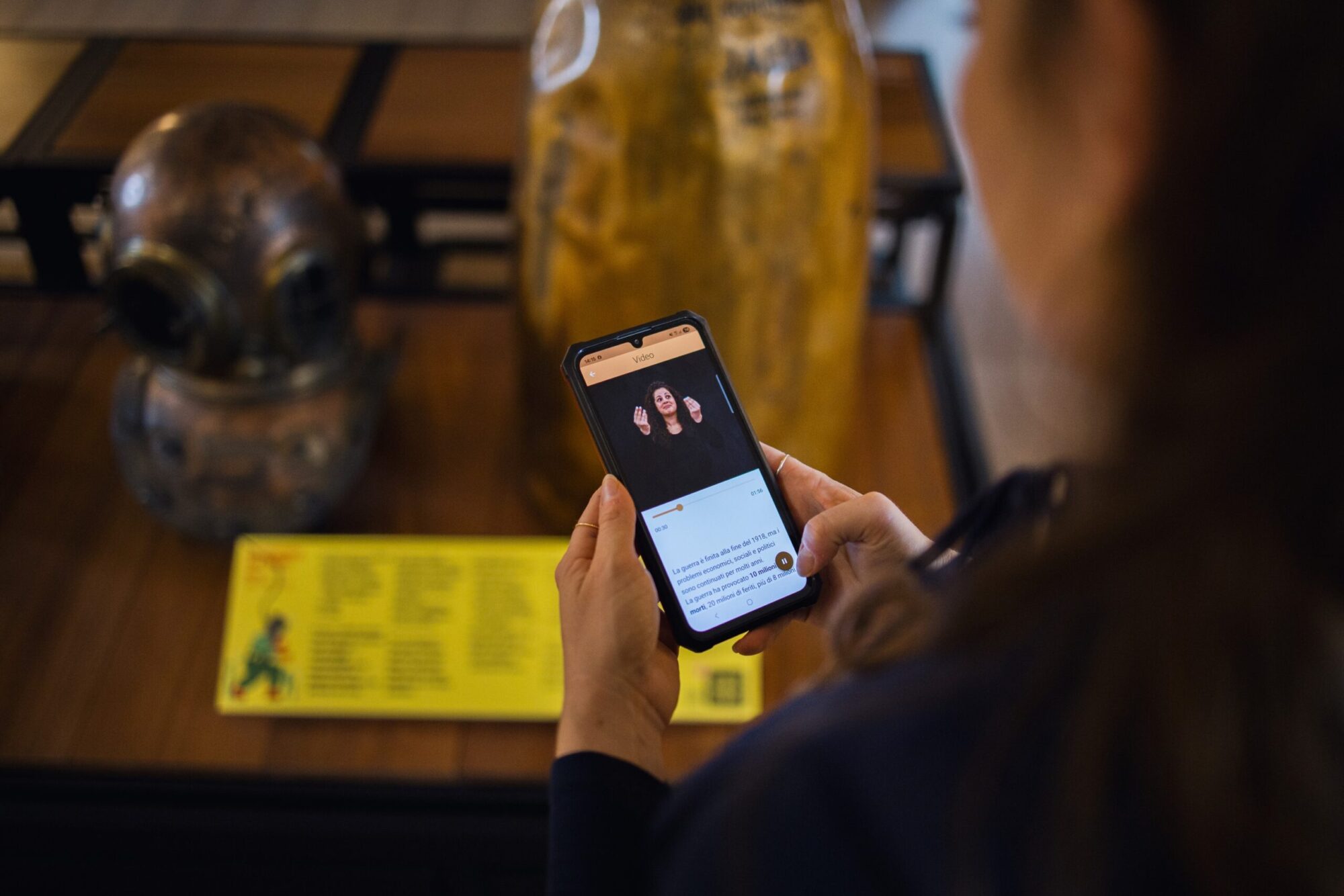 Visitatrice guarda la videoguida in LIS sullo smartphone davanti a una vetrina