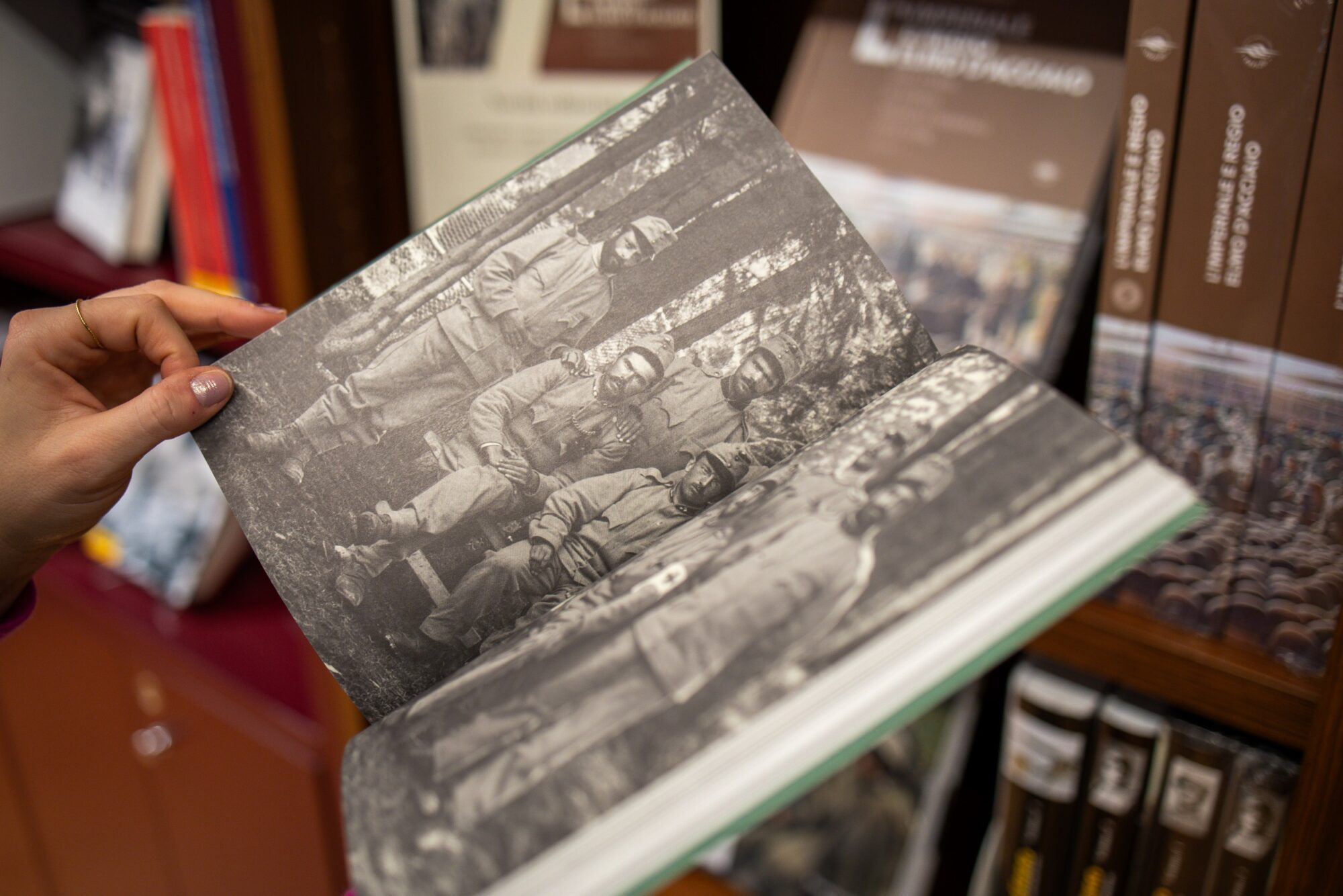 Una mano sfoglia un volume con fotografie storiche tra gli scaffali del bookshop