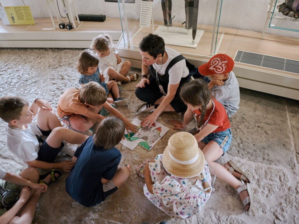 Bambini seduti a terra in cerchio durante una visita per famiglie