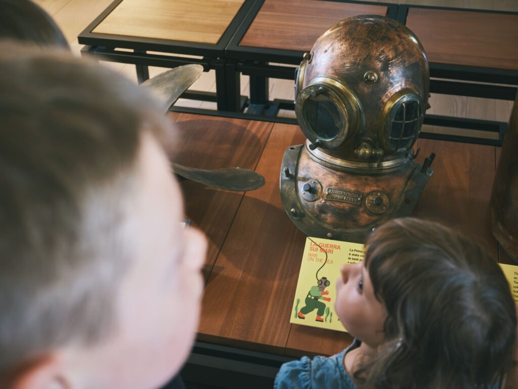Bambini osservano un elmo da palombaro esposto al museo
