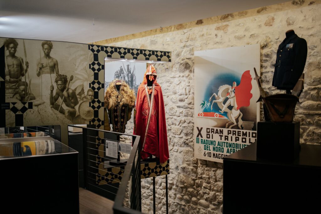 Sala della mostra sul colonialismo italiano con abiti, fotografie e manifesti d'epoca