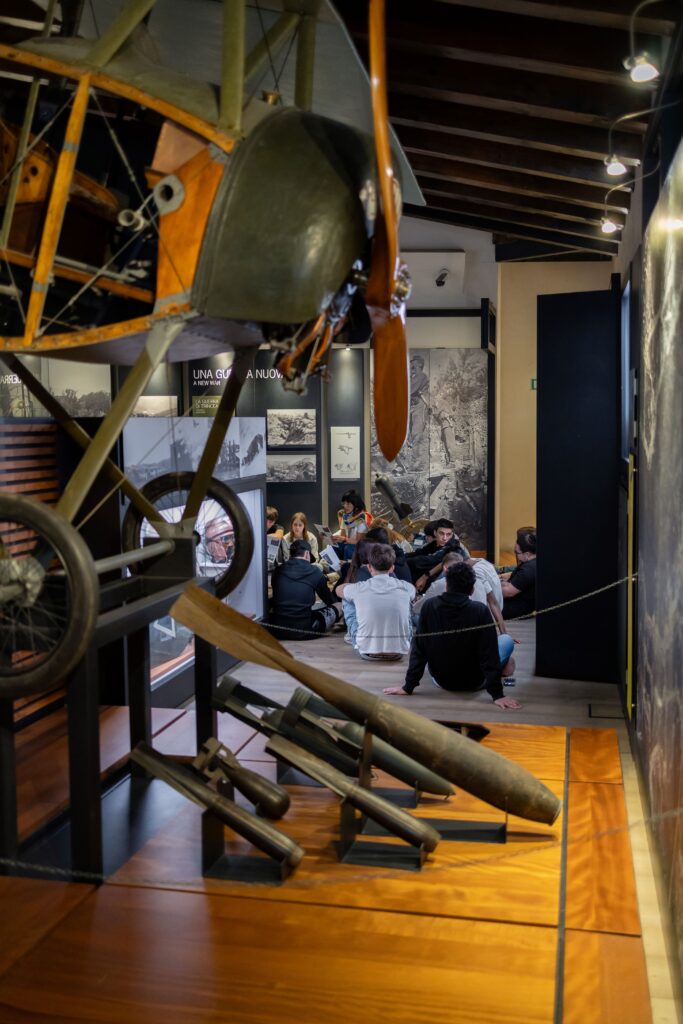 Classe di studenti seduta nella sala dell'aviazione, sotto un aereo d'epoca