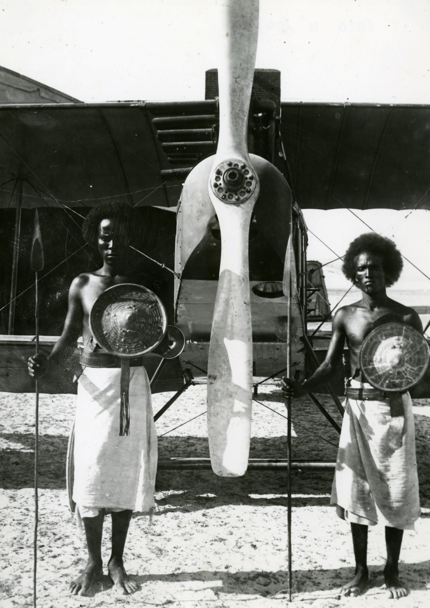 Fotografia storica di due uomini africani con scudi davanti all'elica di un aereo