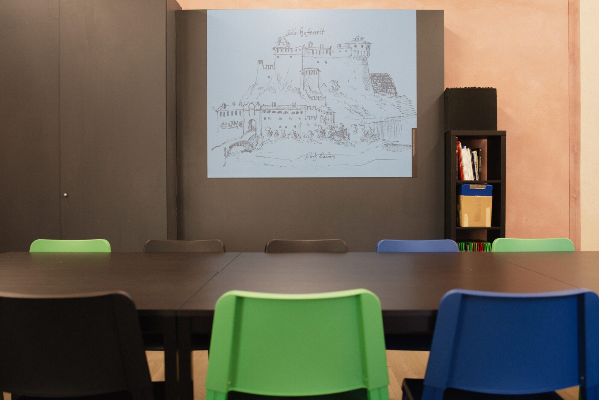 Sala riunioni con tavolo e sedie colorate e un disegno del castello proiettato
