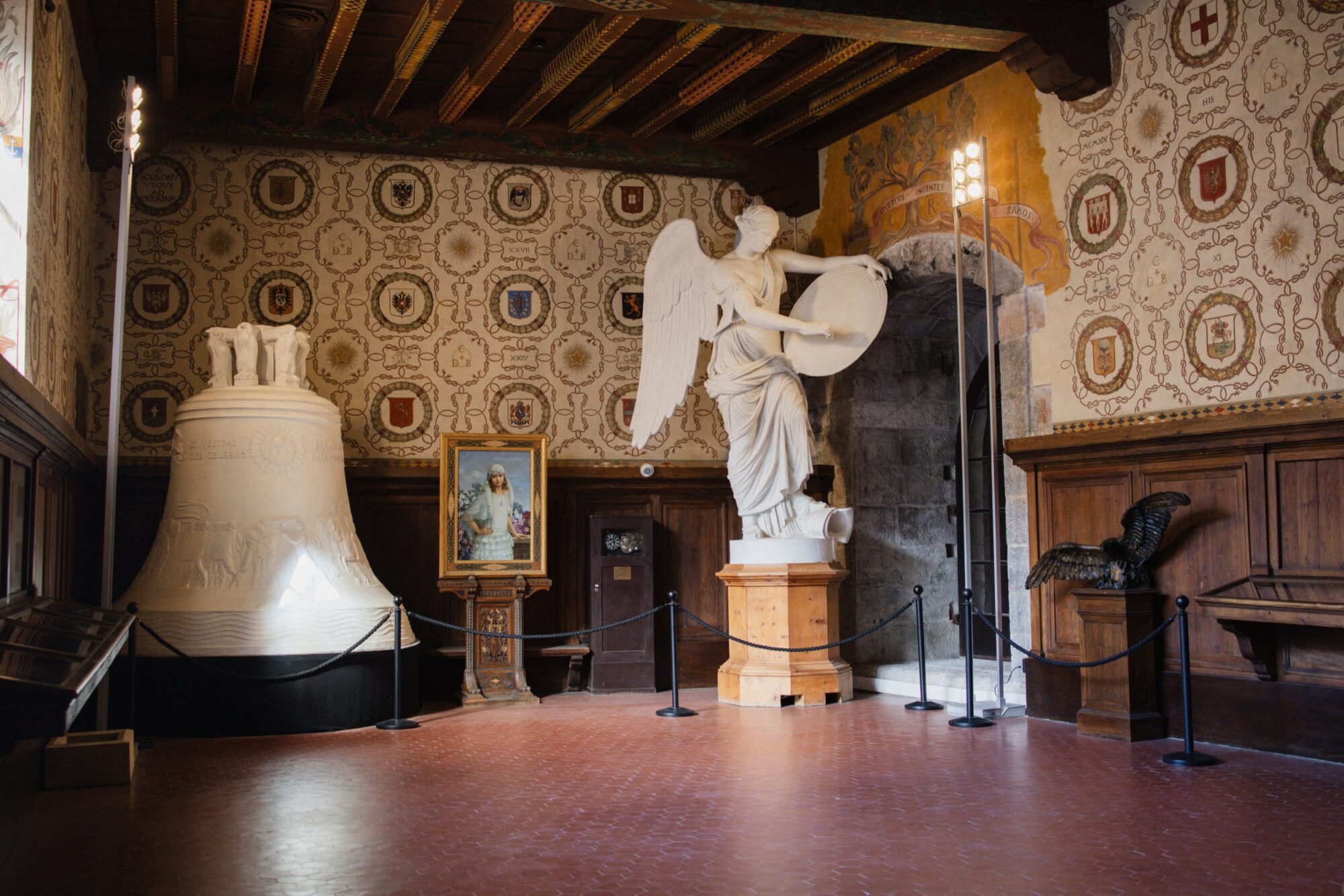 Grande campana e statua di angelo in una sala con soffitto in legno